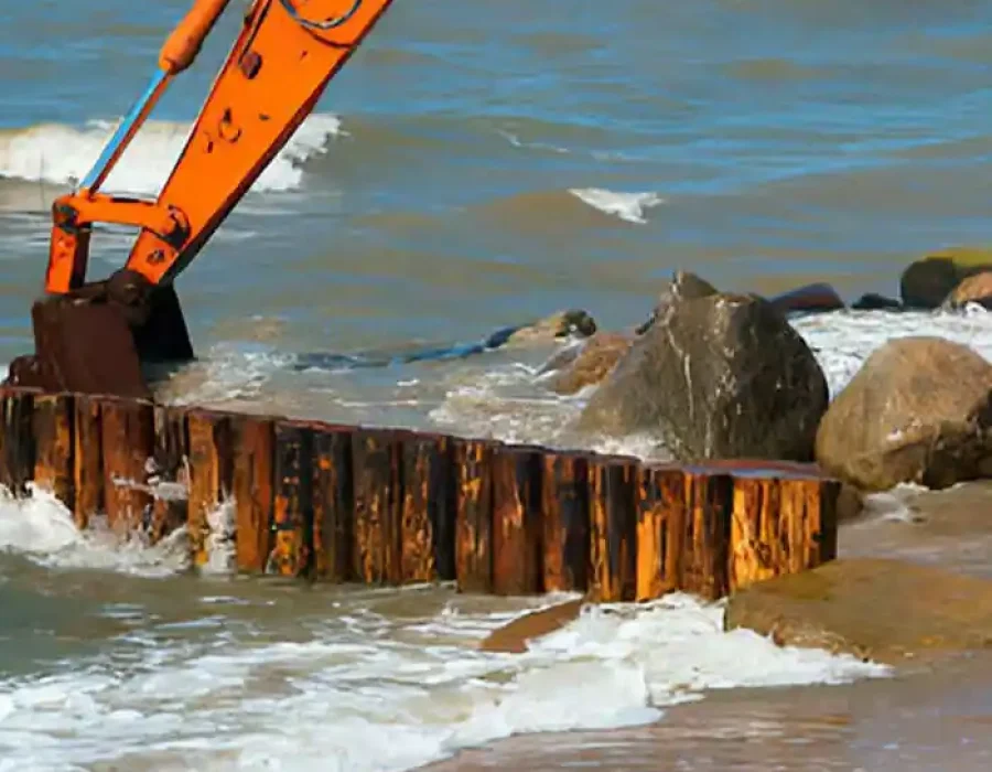 Orange excavator repairing a seawall on a beach to protect against coastal erosion.