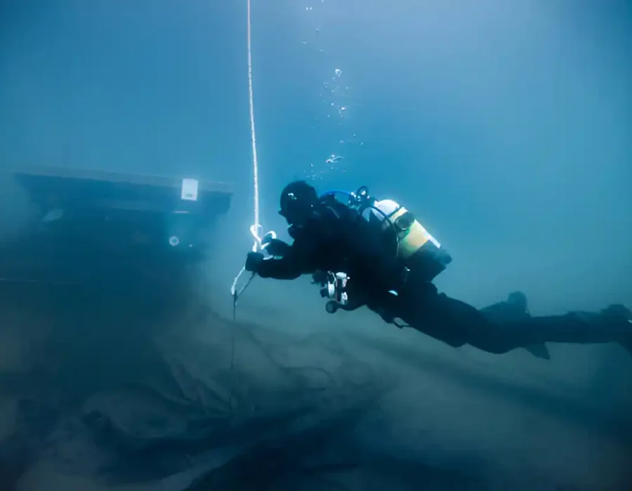 Scuba diver performing underwater structural assessment near submerged equipment