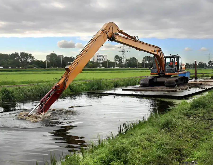 Excavator on floating platform clearing water channel, removing sediment in wetland