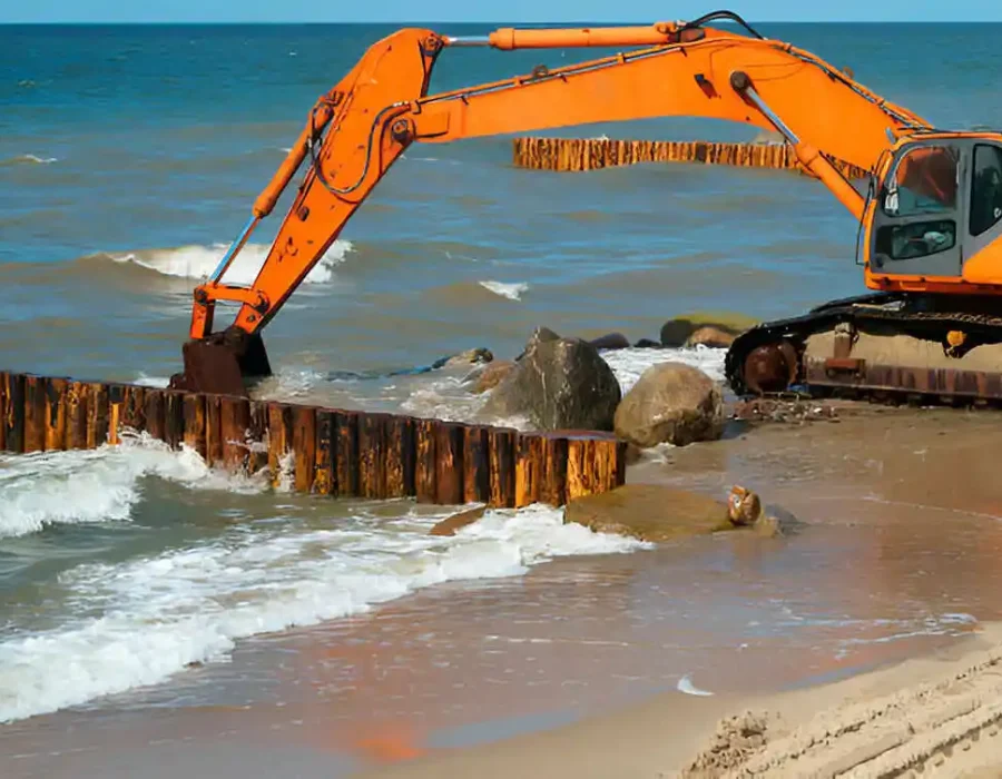 Orange excavator clearing wooden seawall, moving large rocks in marine environment
